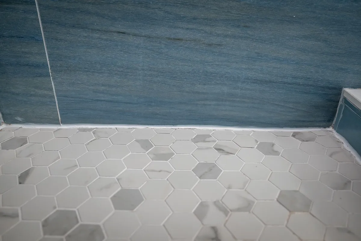 A luxurious bathroom with hexagonal tile flooring and a striking blue marble accent wall, creating a spa-like feel. The space is designed for relaxation and rejuvenation, ideal for unwinding after a day by the ocean.