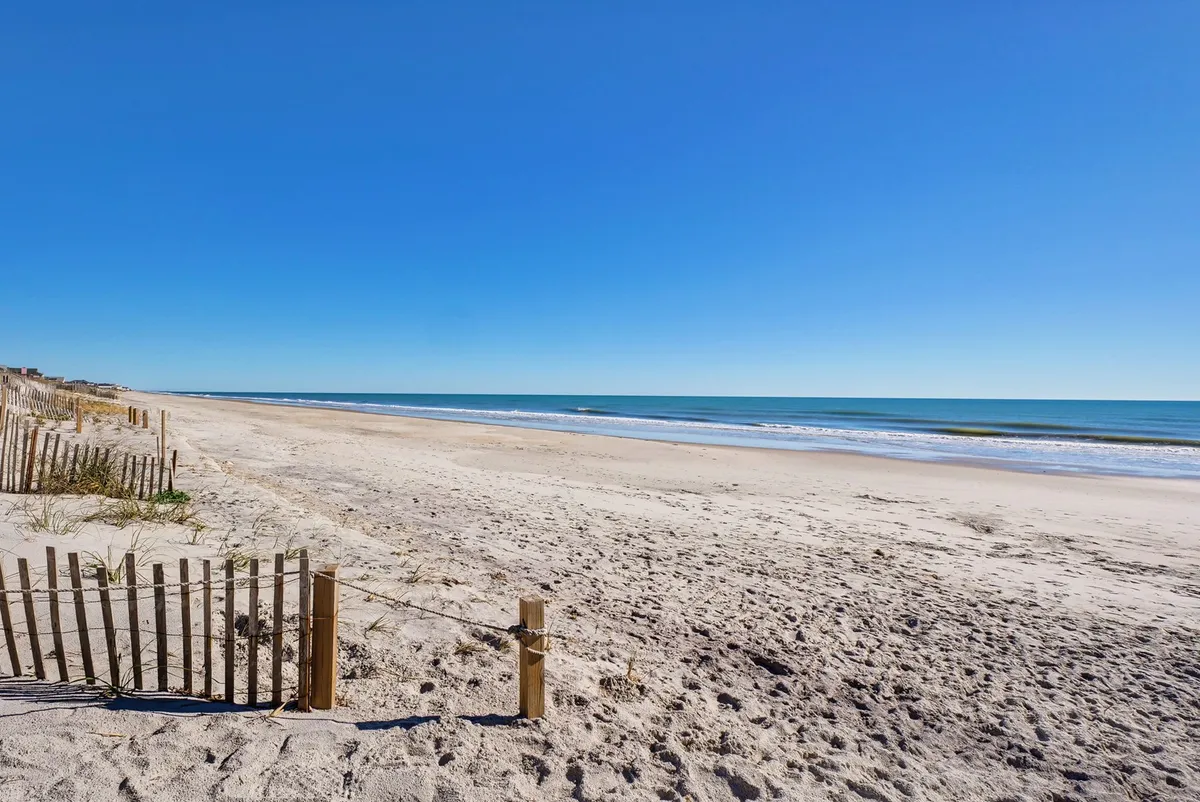 A wide, serene sandy beach bordered by dune fences, with gentle ocean waves rolling in. The open expanse is perfect for long walks, shelling, and enjoying the natural beauty of the North Topsail shoreline in all seasons.