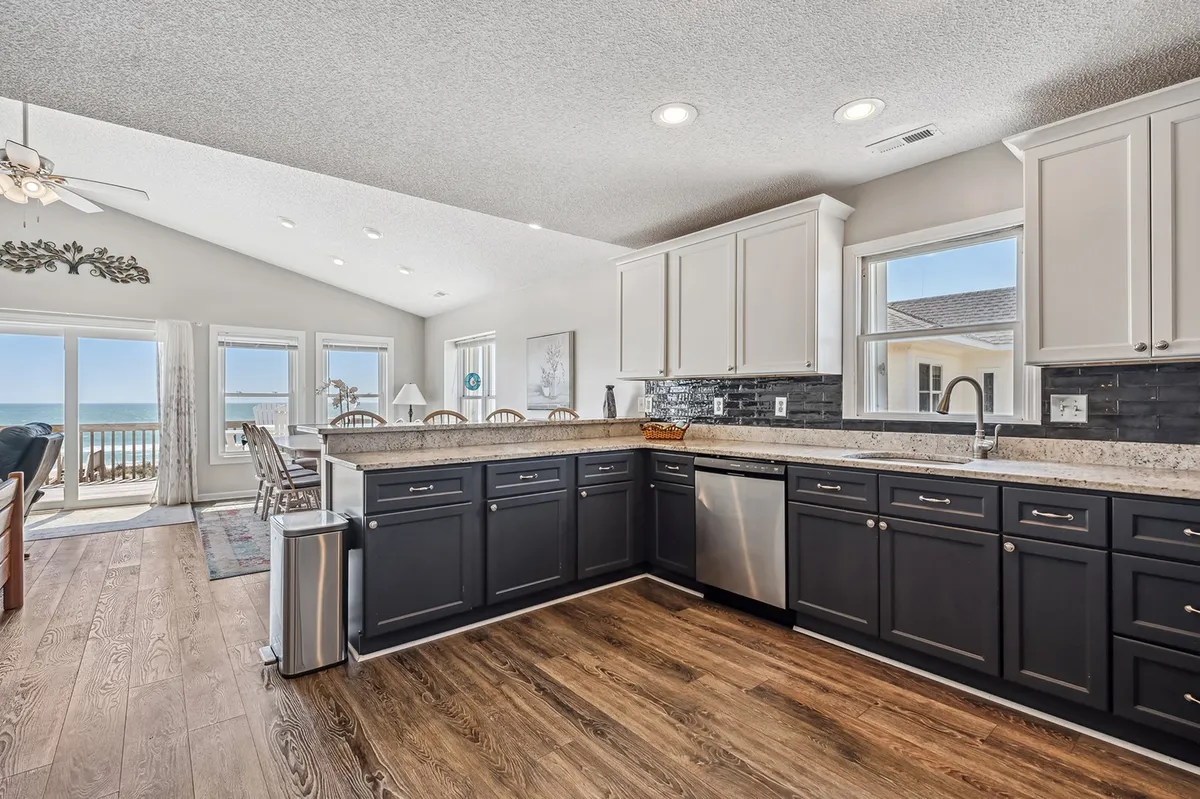 The focus here is a modern kitchen with a central island, sleek cabinetry, stainless steel appliances, and expansive windows showcasing the ocean beyond. The kitchen is bright, inviting, and clearly designed for both meal preparation and social interaction.