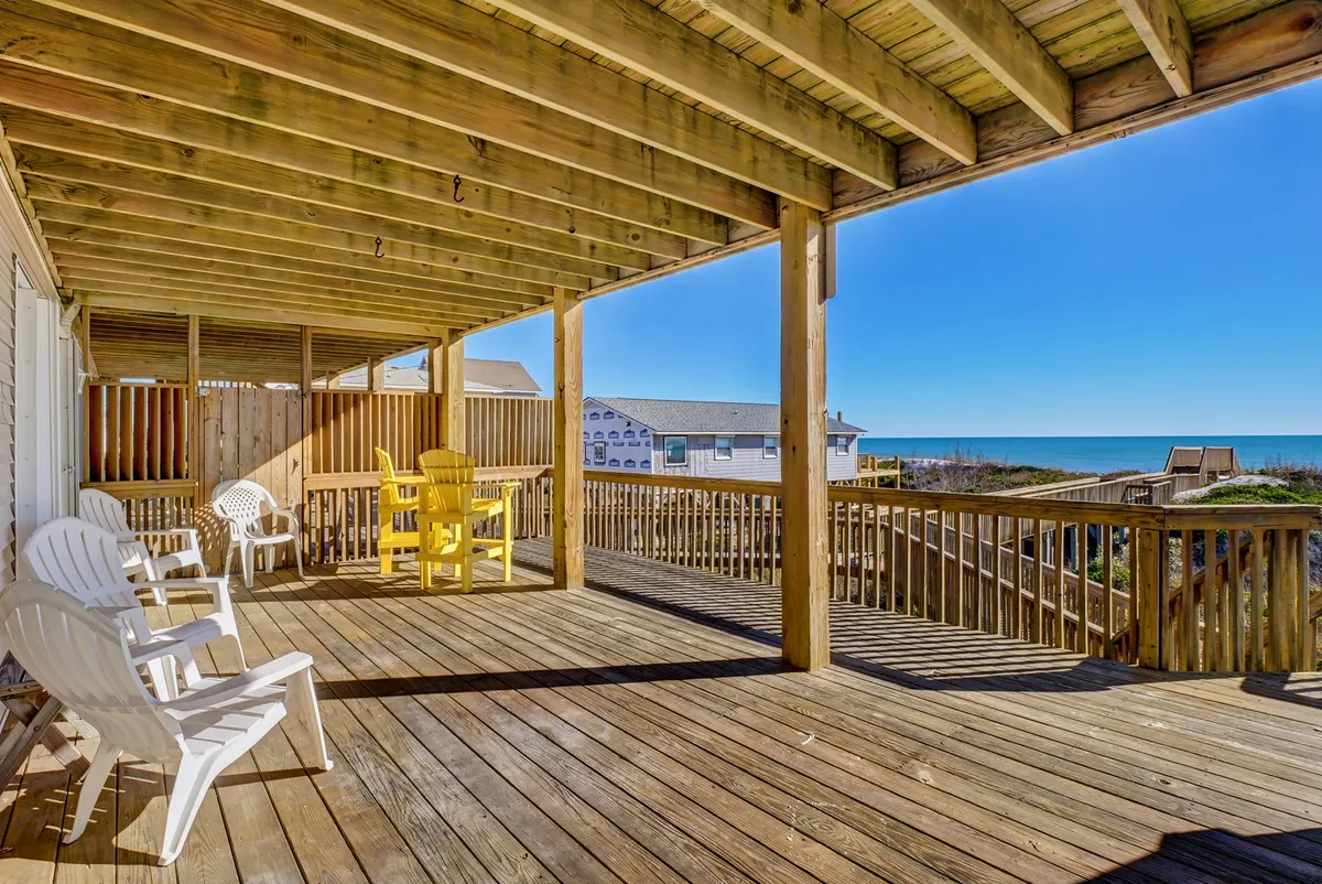 An inviting wooden deck overlooking the ocean, furnished with bright yellow chairs arranged for conversation or relaxation. The vantage point provides sweeping beach views, ideal for social gatherings, beach games, or enjoying a nightcap while listening to the waves.