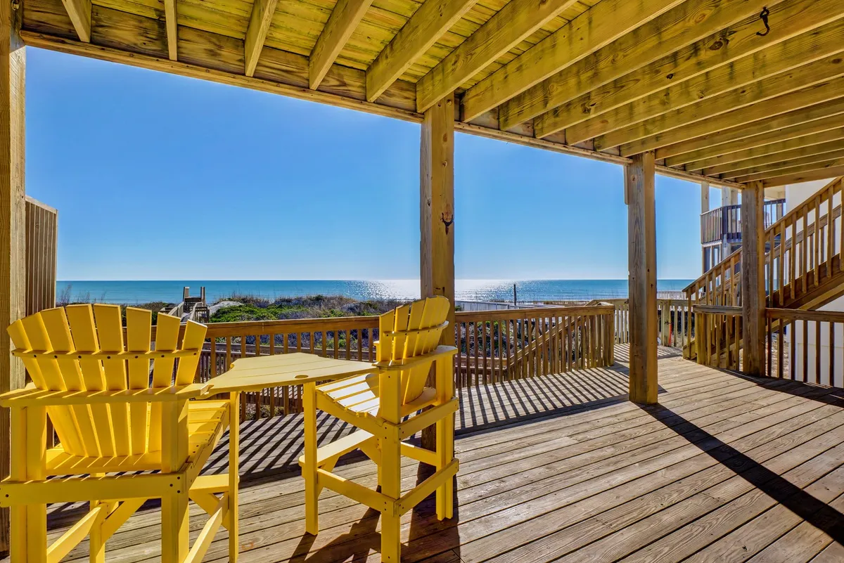 An upper deck scene with yellow chairs set on a wooden deck, overlooking the ocean. The setup invites relaxation, coffee at sunrise, or sunset cocktails, with the sound and sight of waves just beyond the railing.
