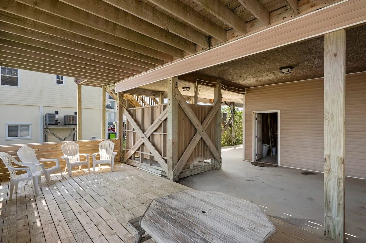 A bright wooden deck with white plastic chairs and a round wooden table, set in an enclosed space with a wooden frame. The area invites relaxation, outdoor dining, and social gatherings with views of the surrounding landscape.