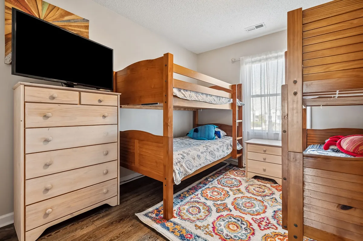 A playful bedroom with bunk beds, a colorful rug, and a dresser topped with a TV. This space feels cozy and inviting, offering room for children or multiple guests to sleep, play, and enjoy entertainment together.