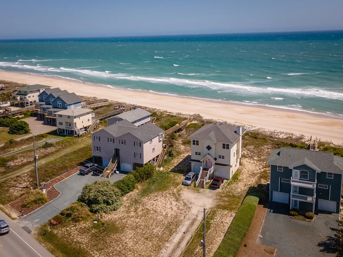 A wide shot of beachfront houses facing the ocean with open sandy beaches and gentle waves. Coastal vegetation adds to the setting, evoking both the vibrancy of local life and the proximity to Surf City’s attractions.