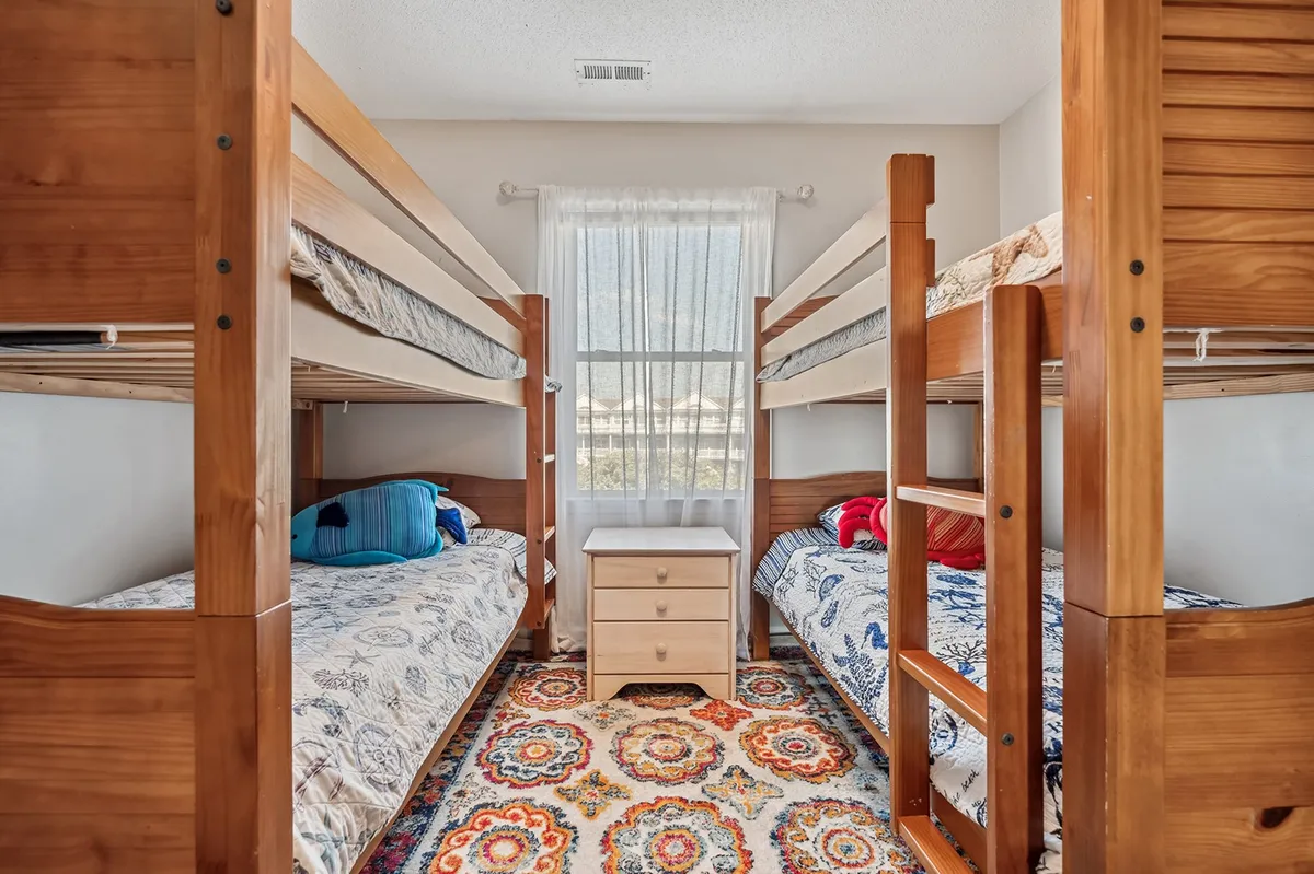 A playful bunk room with twin-over-twin bunk beds, a colorful rug, and a cozy nightstand. The atmosphere is bright and fun, making it an inviting space for children or teens to play, read, or rest.
